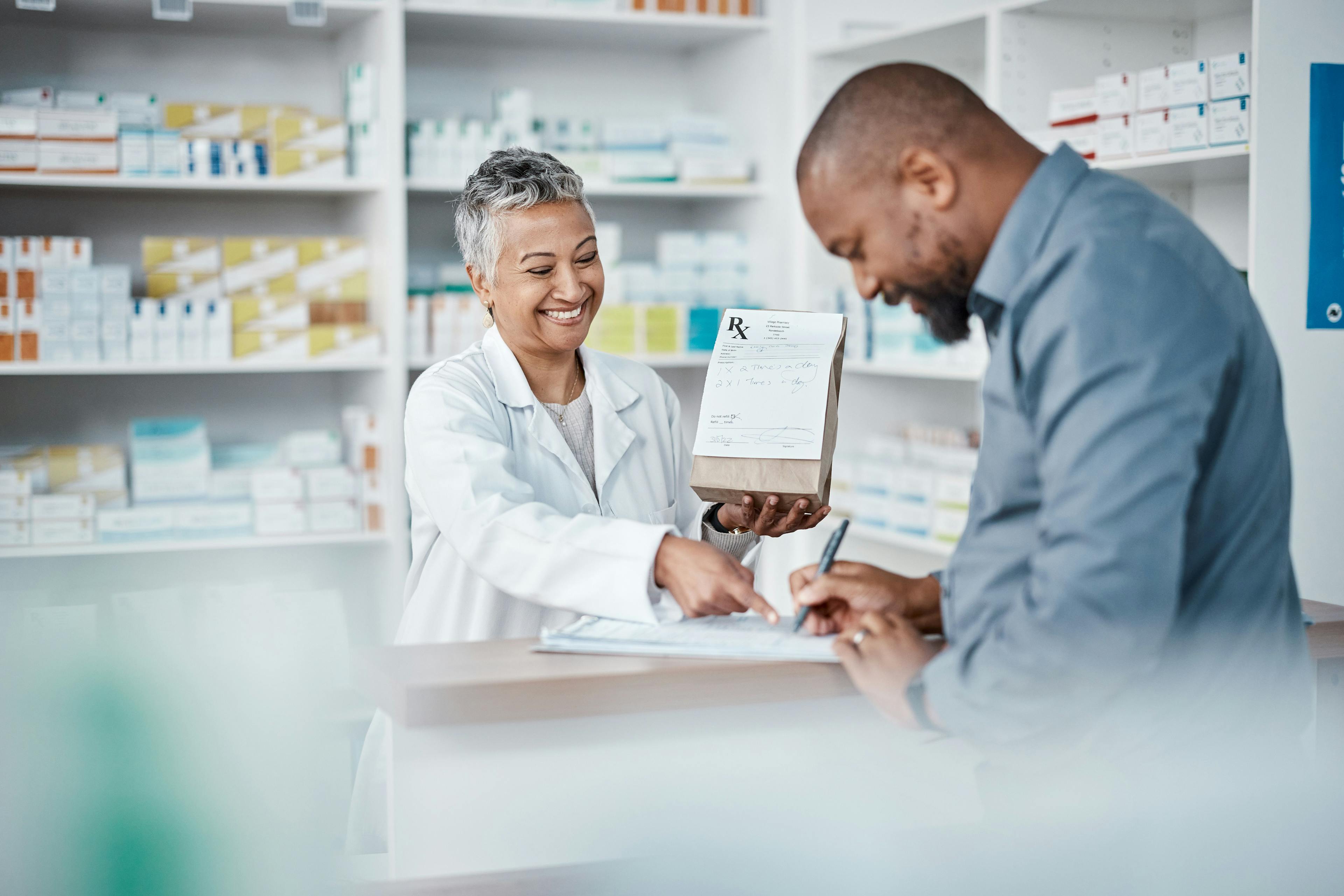 Medicine, shopping or pharmacist with customer writing personal or medical information in pharmacy | Image Credit: C Daniels/peopleimages.com